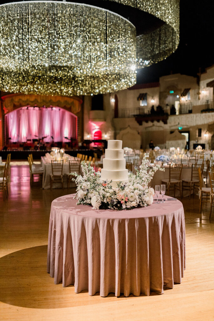 Beautiful florals with 6 tier wedding cake under large chandelier.